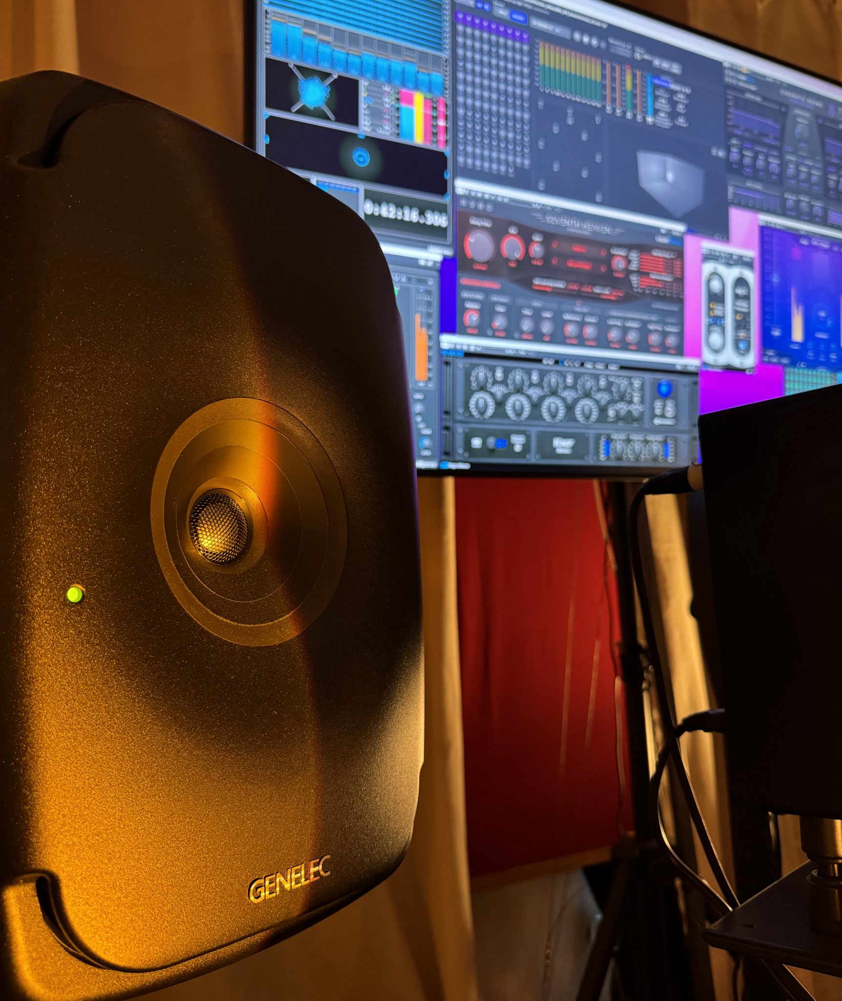 Links eine Genelec Lautsprecherbox für Dolby Atmos im Hintergrund ein Bildschirm mit Mischsoftware